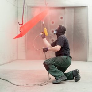 Man applying powder coating to hanging object