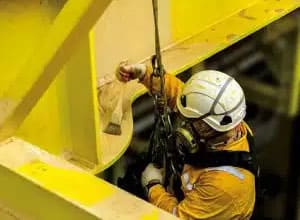 Worker applying protective coating using a harness